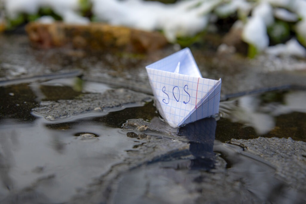A paper boat made of a checkered notebook with the inscription SOS stuck in the ice.